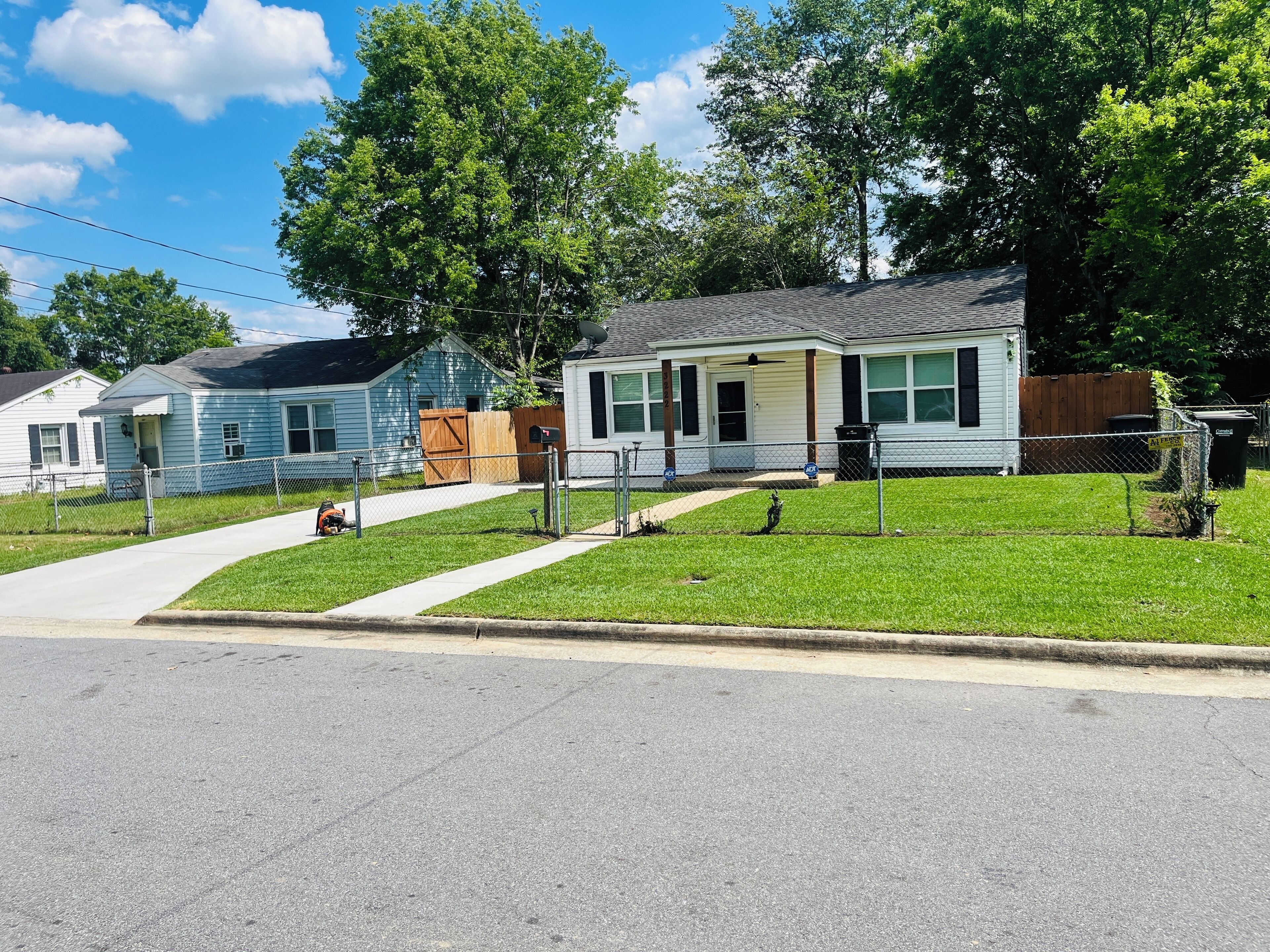 A residential street with two single-story houses, a sidewalk, and a grassy lawn.