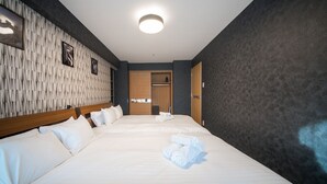 Hotellihuone, jossa on kaksi sänkyä, puinen pääty, pystysuorilla paneeleilla verhoiltu seinä ja ovi, joka johtaa kylpyhuoneeseen.