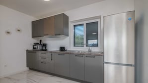 A modern kitchen with grey cabinets, a stainless steel refrigerator, a window with blinds, and a microwave.