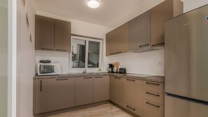Eine moderne Küche mit beigen Schränken, einem Edelstahl-Kühlschrank, einer Mikrowelle und einem Fenster mit Jalousien.