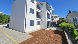 Ein mehrgeschossiges Gebäude mit flachem Dach, weißen Außenwänden und blauen Fensterläden. Klimaanlagen sind an den Außenwänden angebracht.