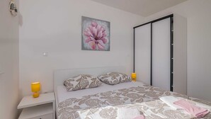 Ein Schlafzimmer mit einem Bett, zwei Nachttischlampen, einem Nachttisch, einer Schublade, einem Blumenbild und einer Schiebetür zum Kleiderschrank.