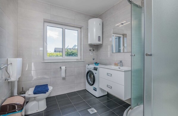 A modern bathroom with a toilet, washing machine, and a window. - Apartment Martina 1 on the ground floor (Malinska)