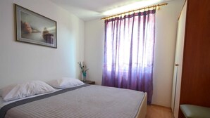 Quarto com cama, mesa de cabeceira, vaso com flores e janela com cortinas.
