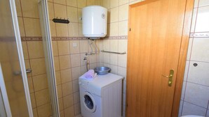 Uma casa de banho pequena com máquina de lavar roupa, chuveiro e sanita.