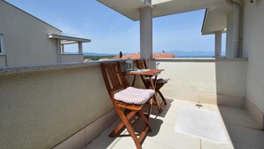 Un balcón con mesa y sillas, vista al mar y suelo de baldosas.