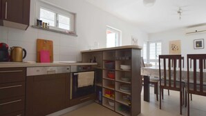 Una cocina moderna con horno empotrado, lavavajillas y tabla de cortar de madera. Hay un comedor con mesa y sillas.