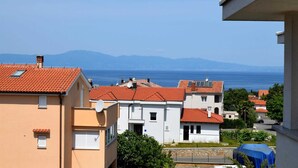 Una zona residencial con tejados de tejas rojas, edificios blancos y color melocotón, y una vista despejada del mar y las montañas al fondo.
