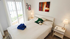A neatly made bed with white linens and two pillows, a bedside table with a lamp, and a painting on the wall.