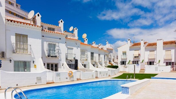 A row of white buildings with balconies, a swimming pool, and a clear blue sky.