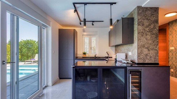 Een moderne keuken met een groot eiland, inbouwapparatuur en uitzicht op een buitenzwembad.