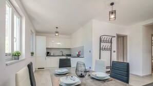 Une cuisine moderne avec des meubles blancs, une table à manger dressée avec des assiettes et des couverts, et un luminaire suspendu.