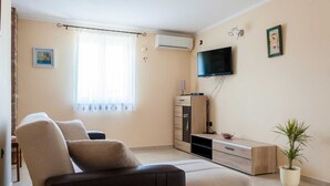 Ein Wohnzimmer mit einer Couch, einem Fernseher und einer Zimmerpflanze.