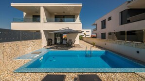 Ein modernes, zweistöckiges Haus mit Swimmingpool, Sitzgelegenheiten im Freien und einer Steinmauer.