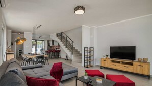 Ein modernes Wohnzimmer mit einer Couch, einem roten Hocker und einem Fernseher auf einem Holzschrank.