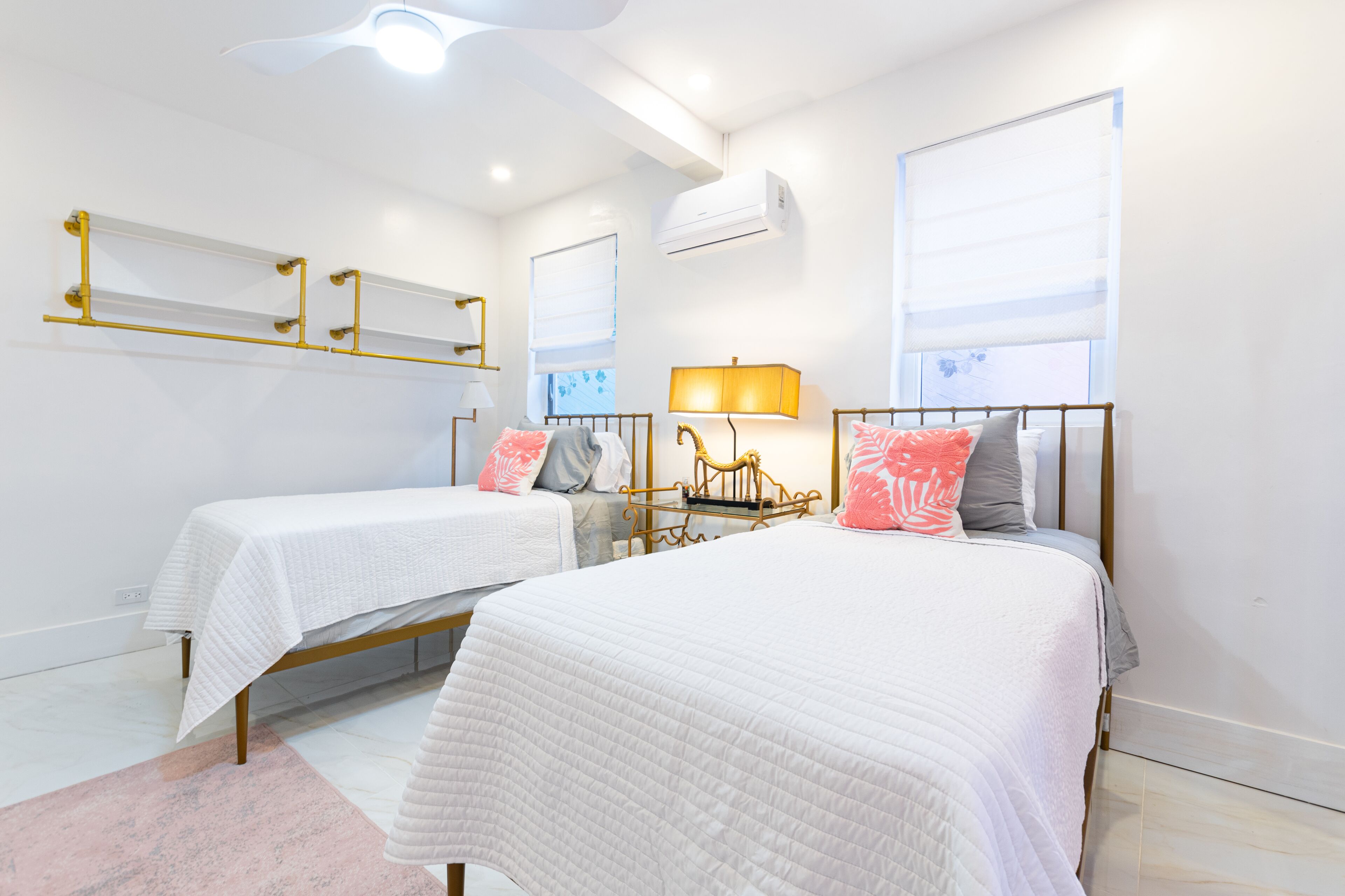 Une chambre avec deux lits, une table de chevet avec une lampe, un miroir et un appareil de climatisation.