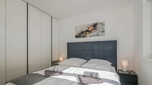 A modern bedroom with a grey and white striped bedspread, two pillows, a grey headboard, and a wall-mounted abstract painting. - Apartment Manuela with private garden and hot whirlpool (Njivice)