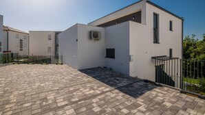 A modern building with a flat roof, a small enclosed patio area, and a brick pathway leading to the entrance. - Apartment Manuela with private garden and hot whirlpool (Njivice)