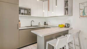 A modern kitchen with a central island, white bar stools, and a hanging light fixture. - Apartment Manuela with private garden and hot whirlpool (Njivice)