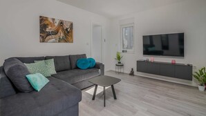 A modern living room with a grey sofa, a coffee table, and a flat-screen TV mounted on the wall. - Apartment Manuela with private garden and hot whirlpool (Njivice)