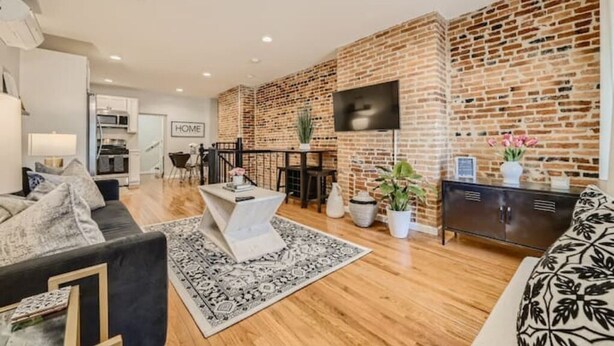 Un salon moderne avec un mur en briques, un téléviseur à écran plat, un coin repas et un canapé.