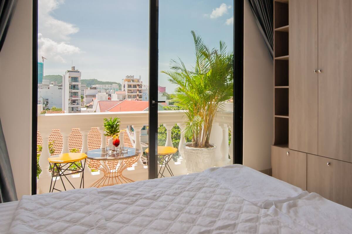 Camera d'hotel con un letto grande, un balcone con tavolo e sedie, e vista sulla città.