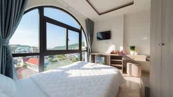 A hotel room with a large bed, a TV mounted on the wall, a desk with a plant, and a view of the city.