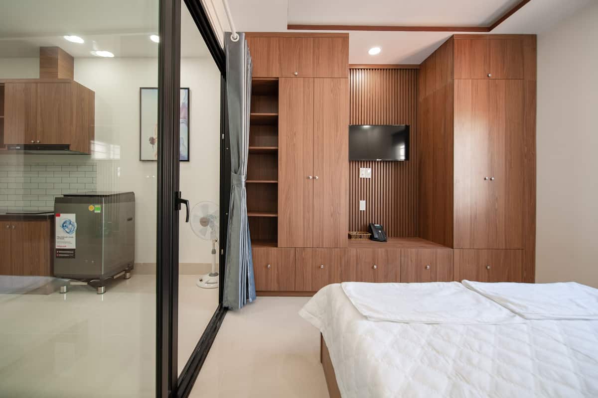 Una camera da letto con un letto, un'armadio in legno, una TV montata a parete e un angolo cottura con frigorifero e microonde.