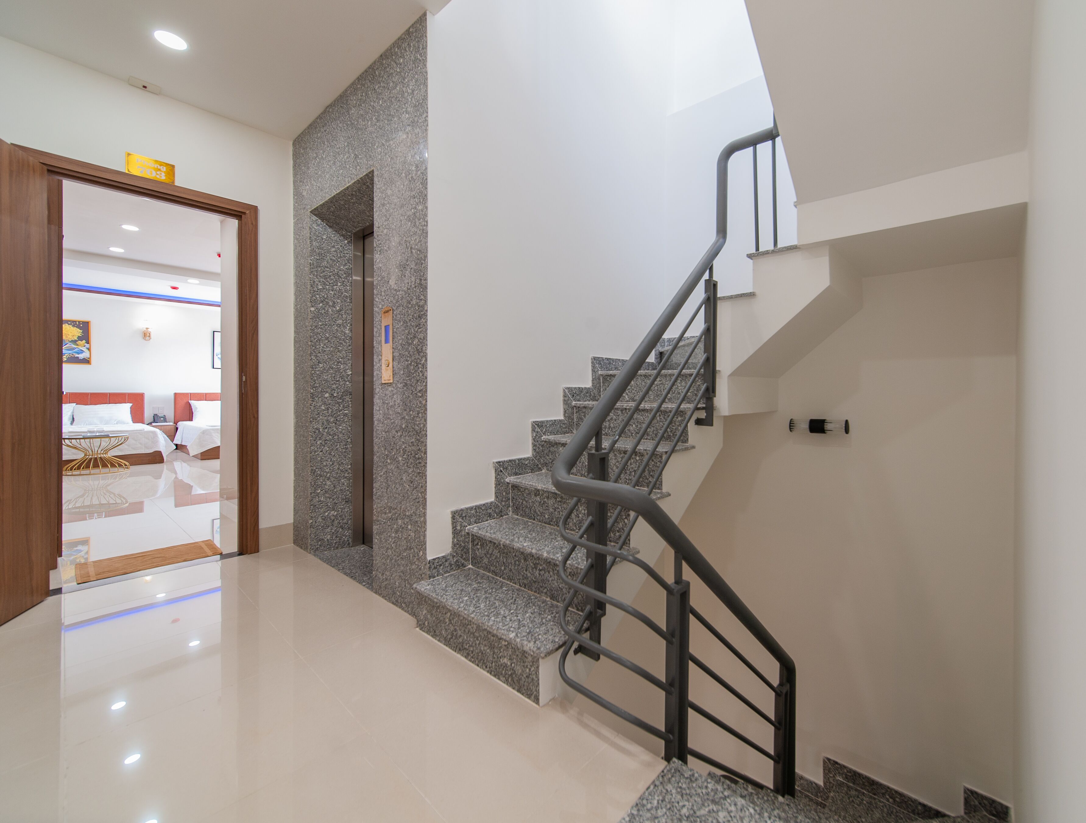 A modern hotel interior with a staircase, a wooden door leading to a room, and a clean, polished floor.