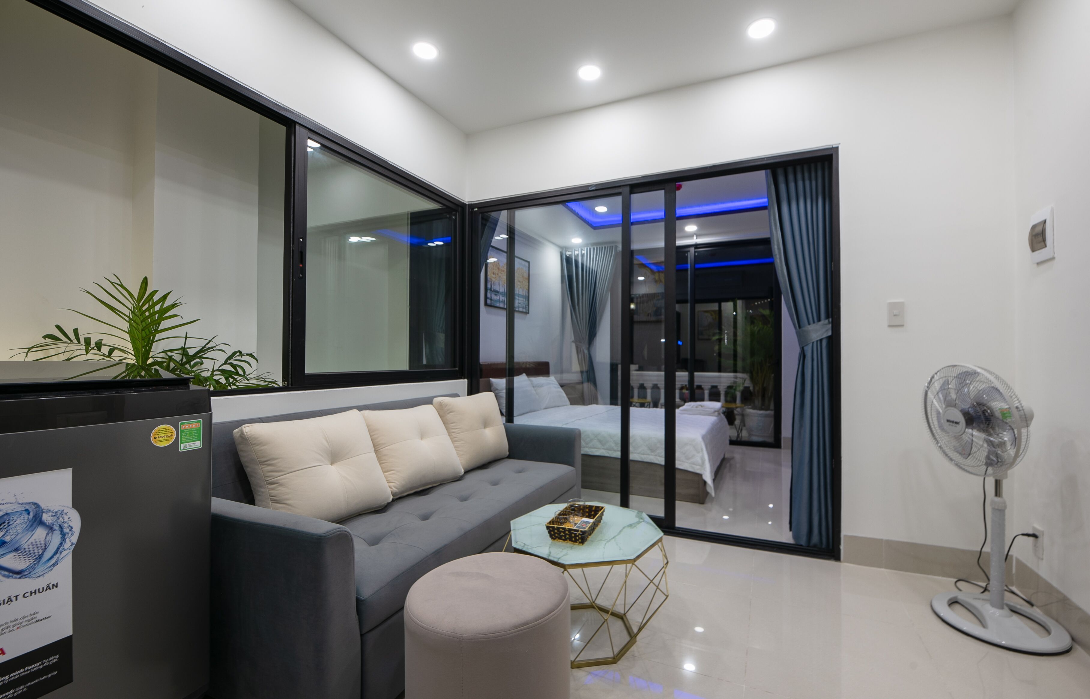 A modern living room with a sofa, a glass partition, and a fan.