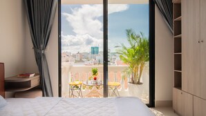 Un dormitorio con cama, escritorio, silla, mesa con planta y balcón con vista a la ciudad.