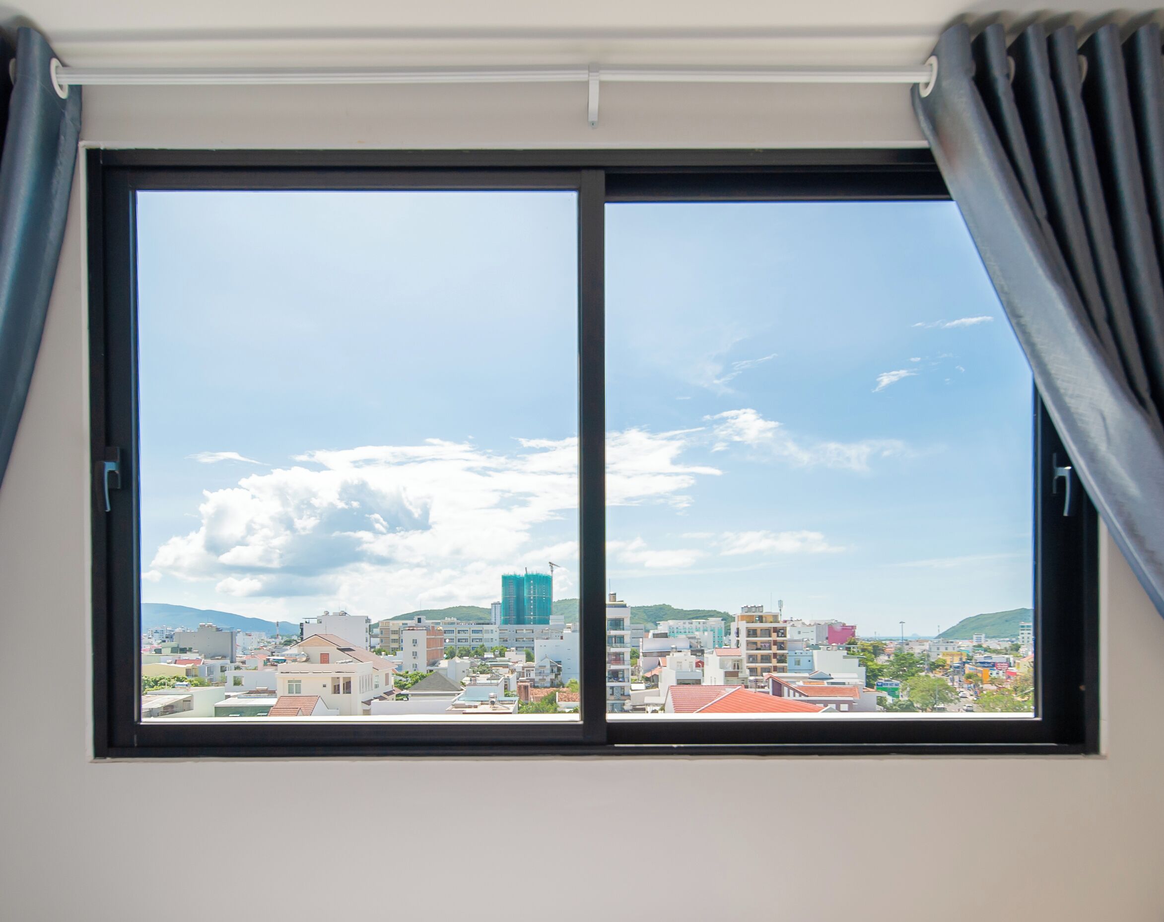 Un amplio ventanal con vistas a un paisaje urbano, que incluye edificios y una montaña.