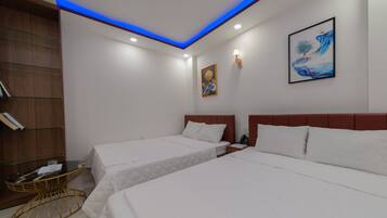 A hotel room with two beds, a small table, a bookshelf, and a painting on the wall.