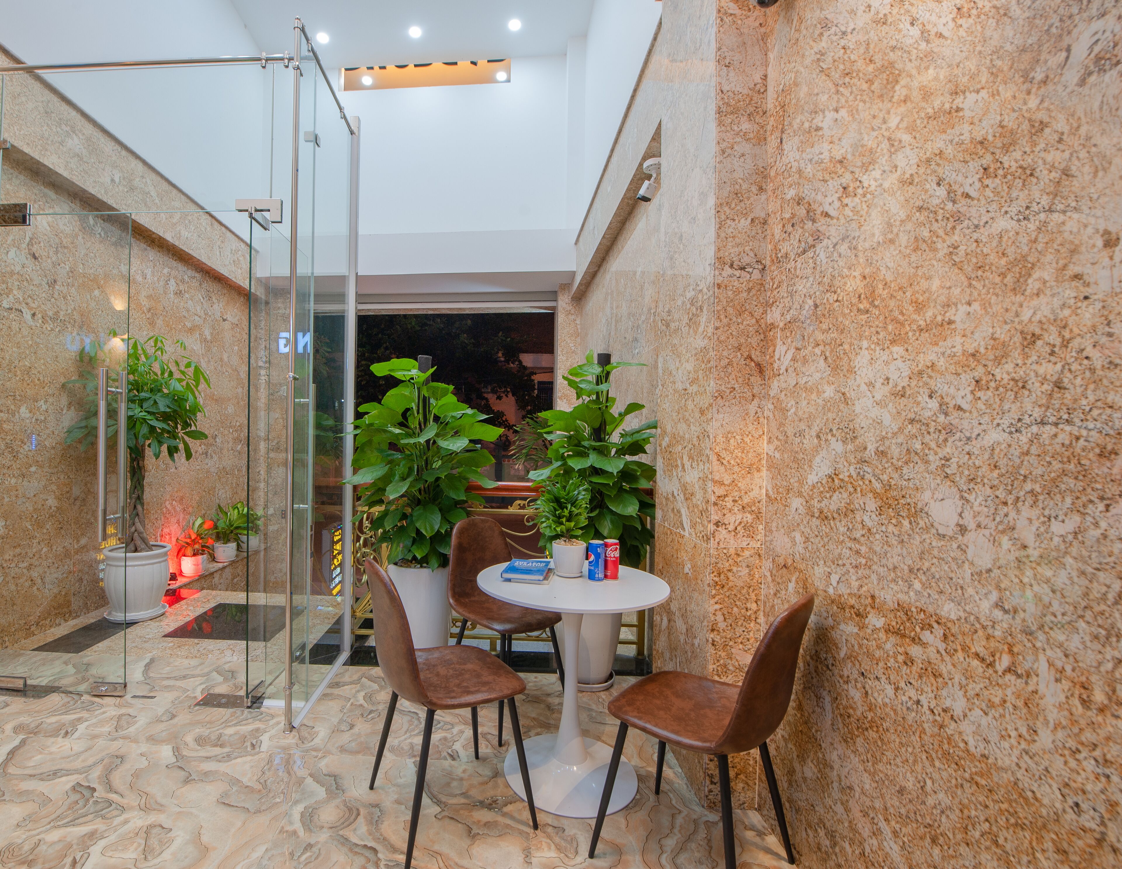 A modern interior with a glass partition, a round table with chairs, and potted plants.