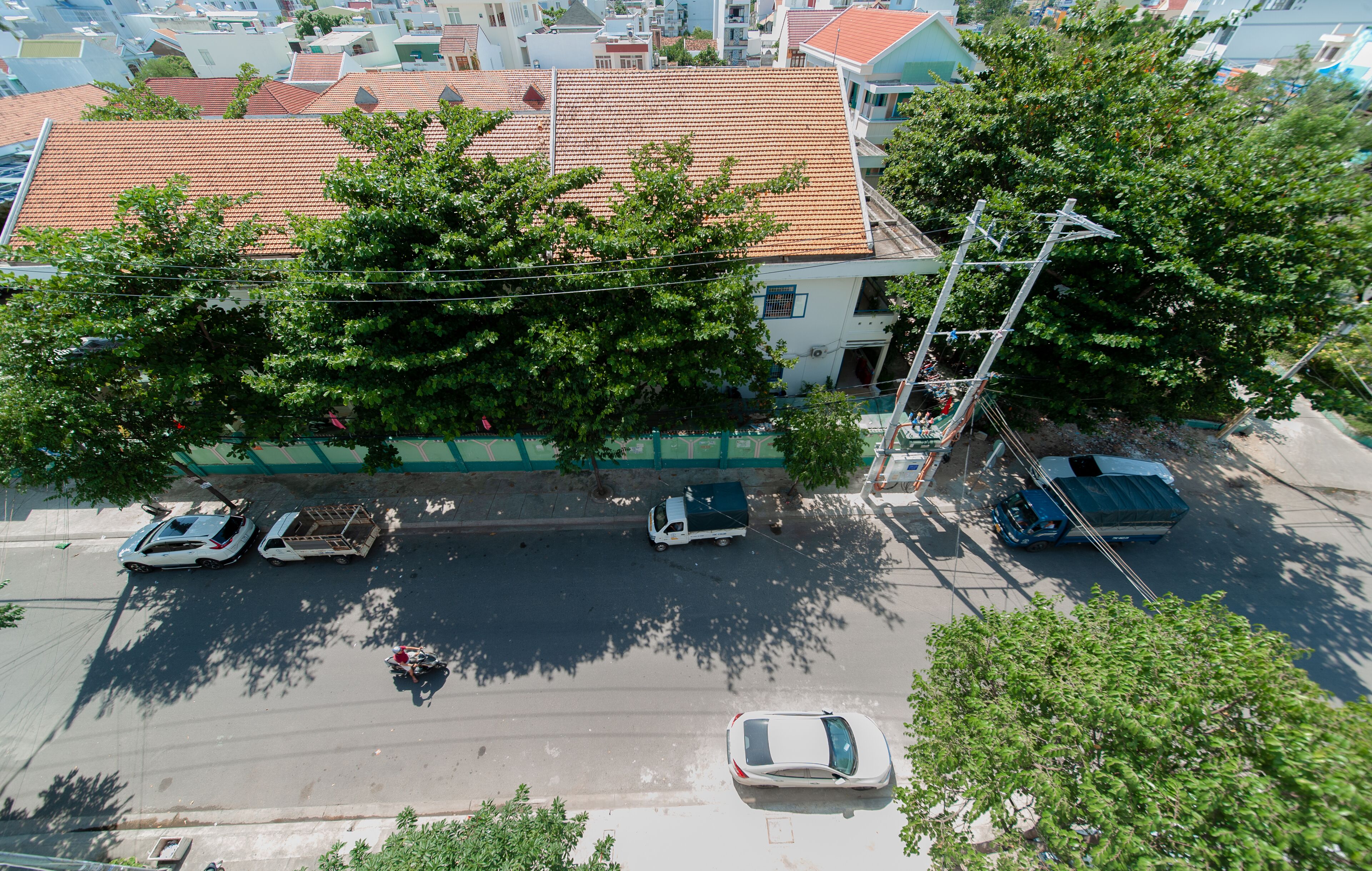 An aerial view of a street with parked cars, a motorcycle, and a building with a tiled roof.