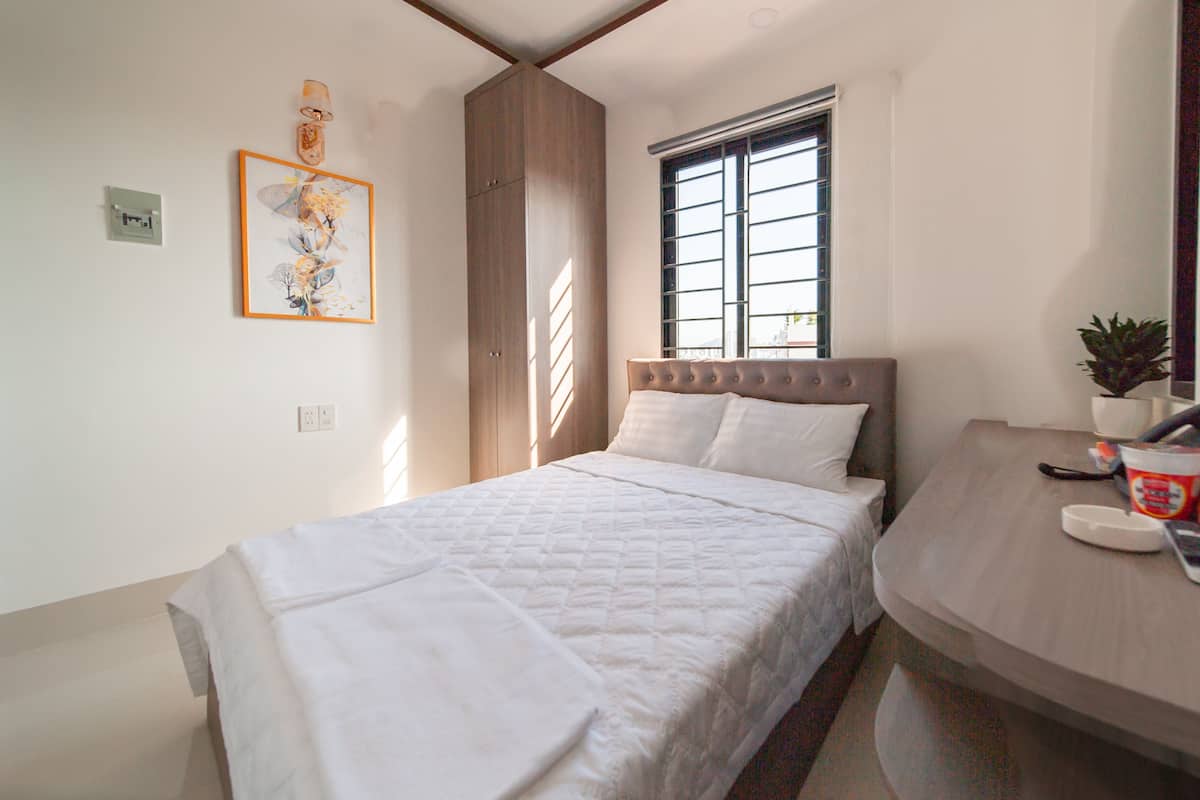 Una camera da letto con un letto, una finestra con persiane, un comodino con una pianta e un lampadario a parete.