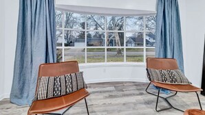 A room with a bay window, two brown chairs with patterned cushions, and blue curtains. - The Mid-Century Retreat (Lansing)