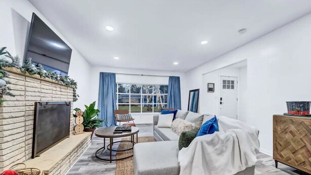 A modern living room with a fireplace, a sofa, a coffee table, and a TV mounted on the wall. - The Mid-Century Retreat (Lansing)