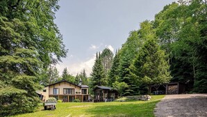 Kaksikerroksinen talo, jossa on suuri etupiha, katettu ulkotila oleskelua varten ja sorapäällysteinen ajotie.