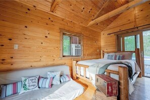Relax in this cozy cabin-style room with two beds, a wooden bench, and a sloping ceiling with exposed beams.