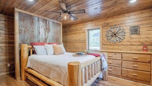 A wooden cabin bedroom with a bed, a dresser, a wall clock, and a ceiling fan. - Buffalo County Log Cabin w Guesthouse and pool (Alma)