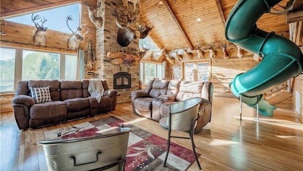 A log cabin interior with a fireplace, leather sofas, a green slide, and deer antlers on the walls. - Buffalo County Log Cabin w Guesthouse and pool (Alma)