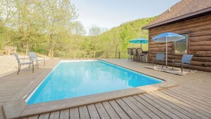 A wooden deck with a rectangular pool, surrounded by lounge chairs and umbrellas. - Buffalo County Log Cabin w Guesthouse and pool (Alma)