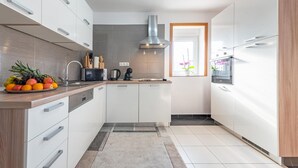 A modern kitchen with white cabinets, a stainless steel range hood, a microwave, and a coffee maker. - Amazing apartment in Gracac (Gracac)