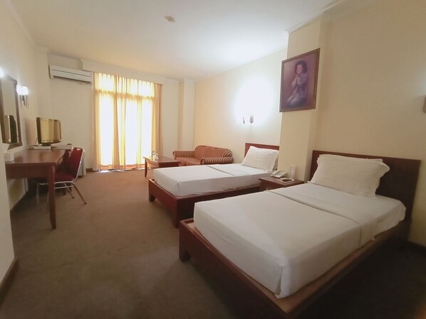 A hotel room with two beds, a desk, a chair, a TV, and an air conditioning unit.