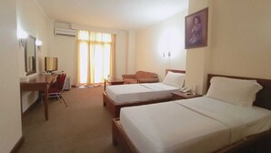 Una habitación de hotel con dos camas, un escritorio con silla, televisión y ventana con cortinas.