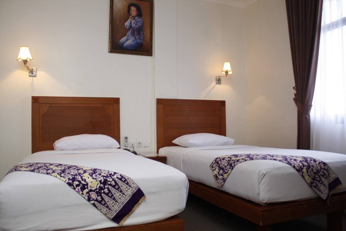 Deux lits simples avec des têtes de lit en bois, du linge de lit blanc et des plaids à motifs violets.
