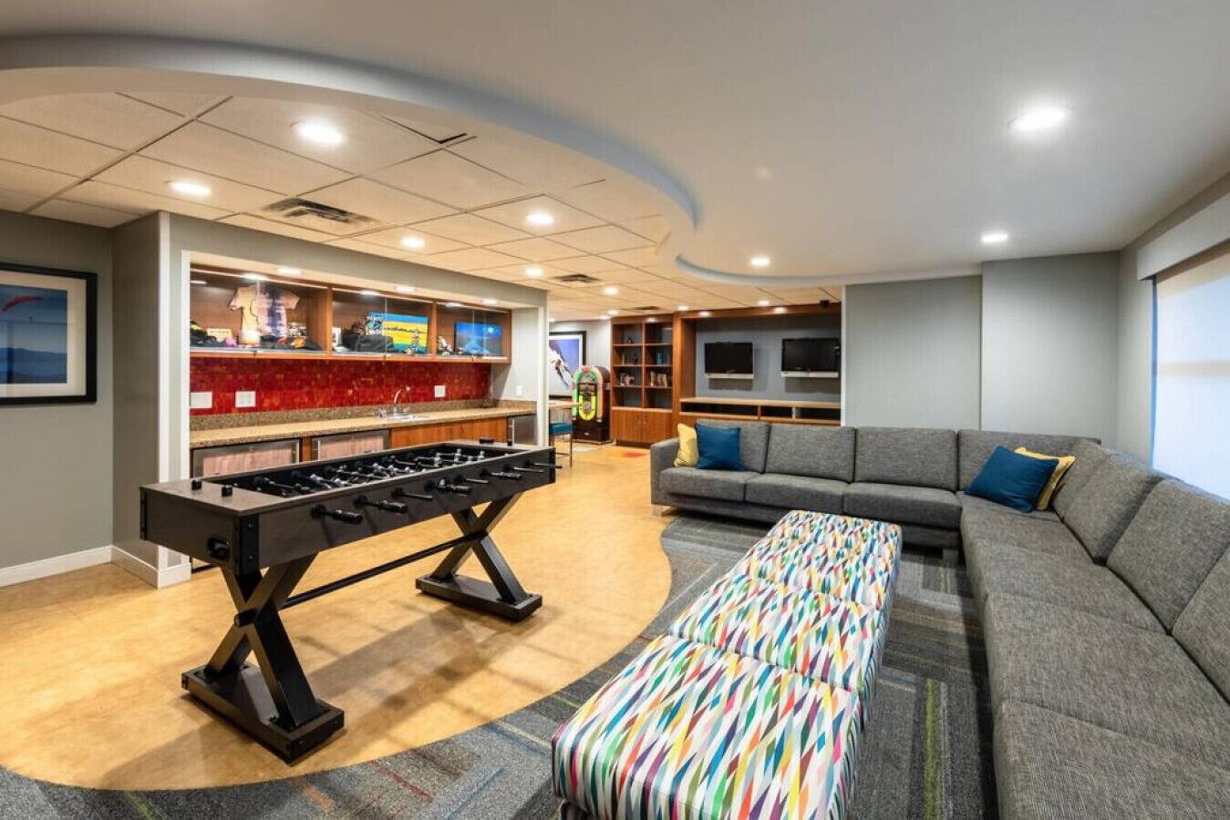 Una sala de estar moderna con una mesa de fútbol de mesa, un sofá y un otoman colorido.