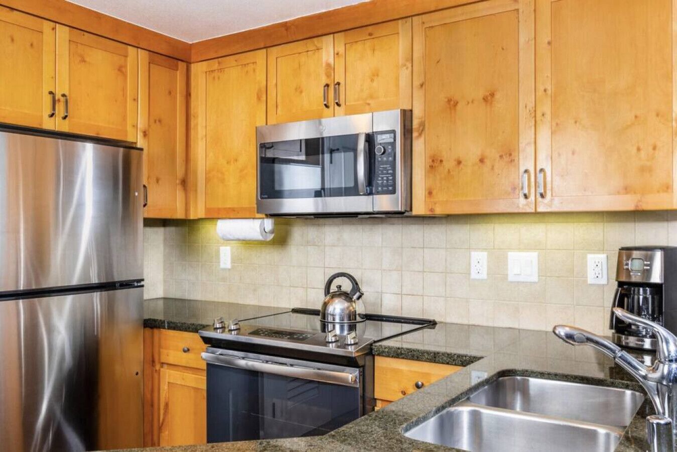 Una cocina con armarios de madera, electrodomésticos de acero inoxidable, una tetera y una cafetera.