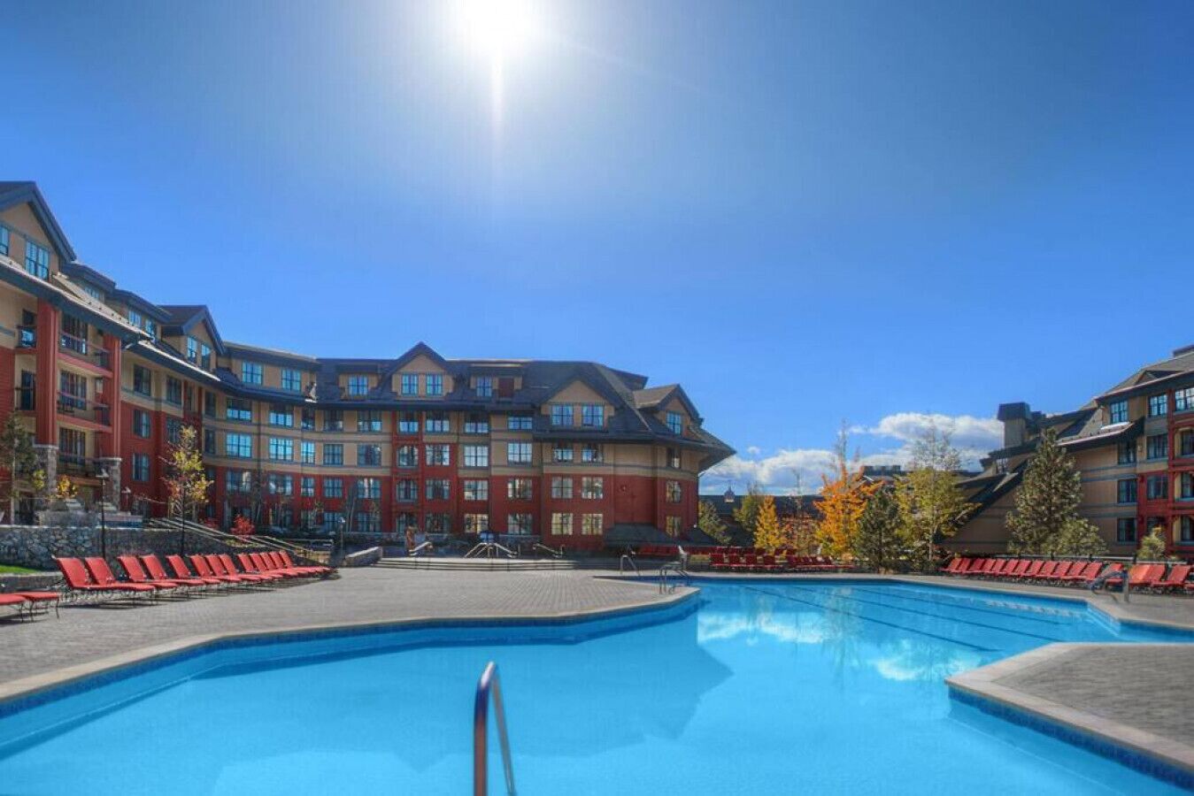 A hotel with a large pool, red chairs, and a clear blue sky.